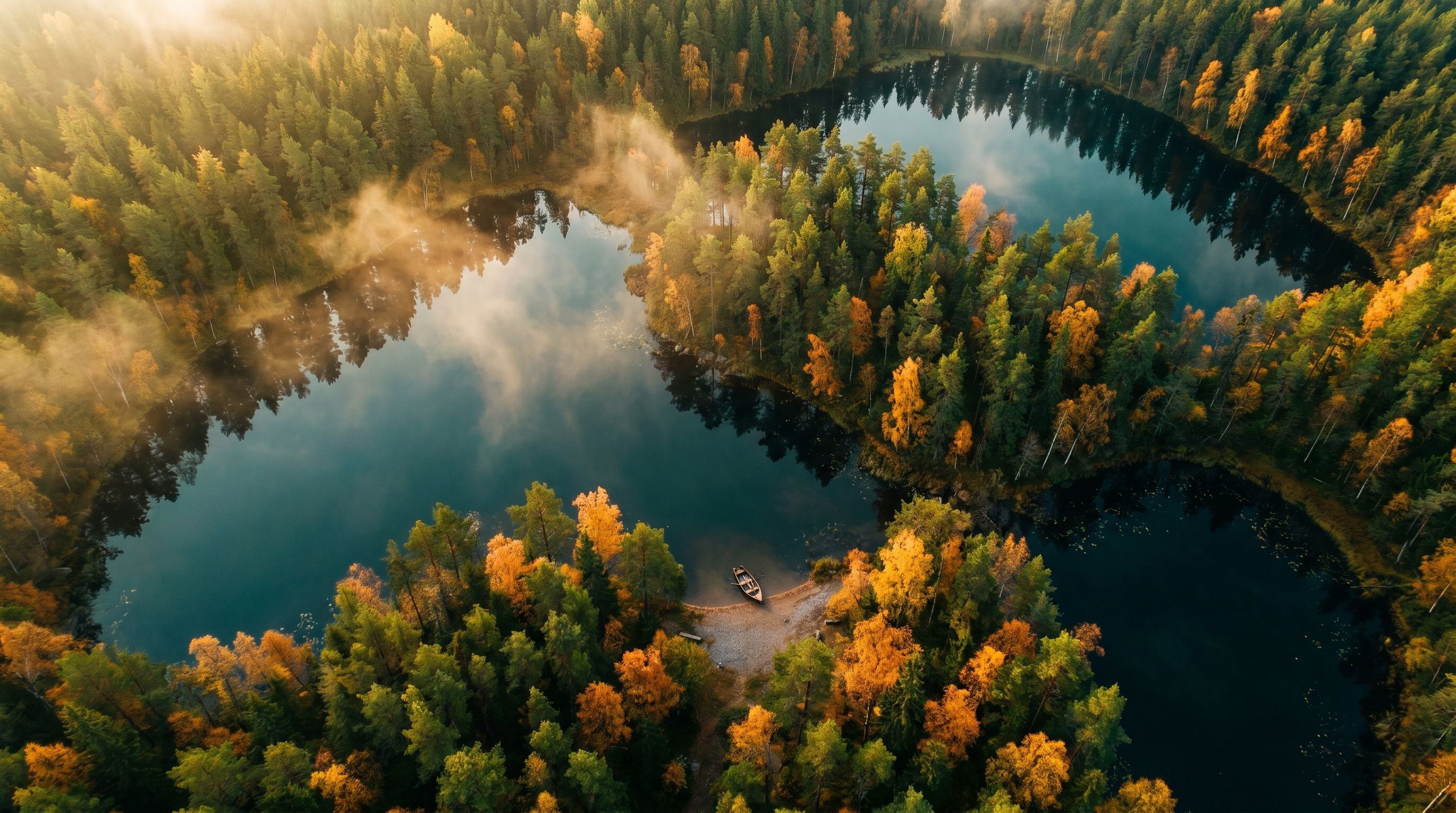 Flygvy över en svensk skogssjö omgiven av höstgyllene tallar och mistlandskap.
